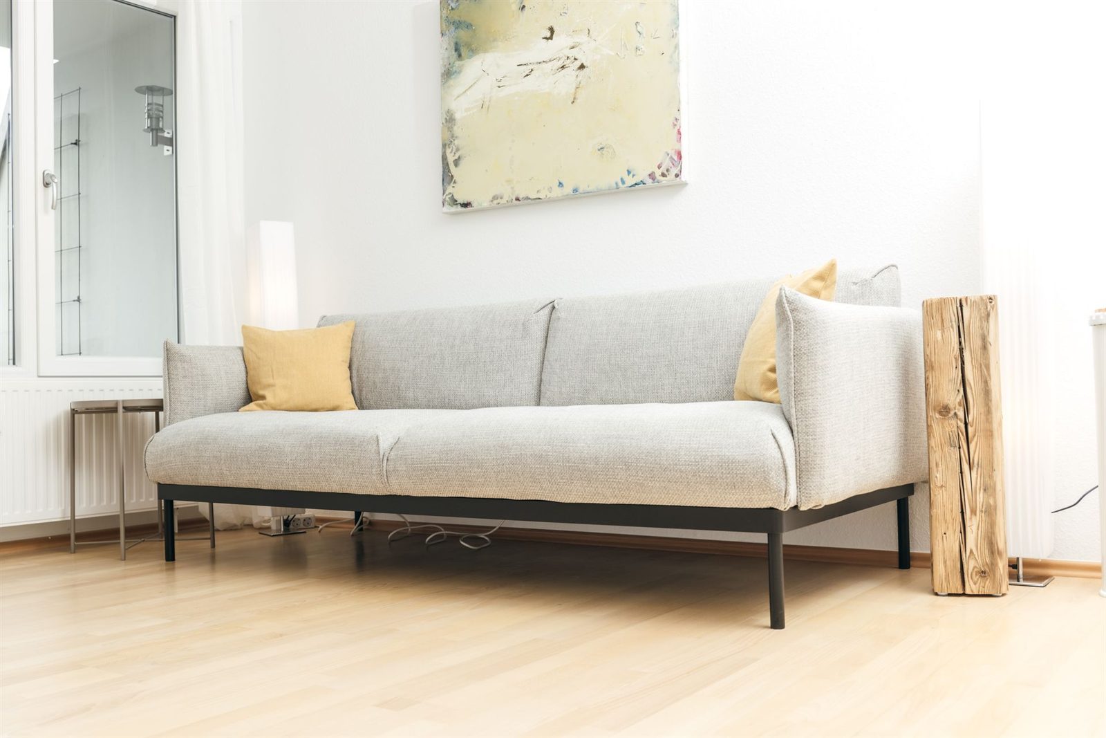 Wohnzimmer · Sofa mit Aquarell darüber, links geht es zum Bad
