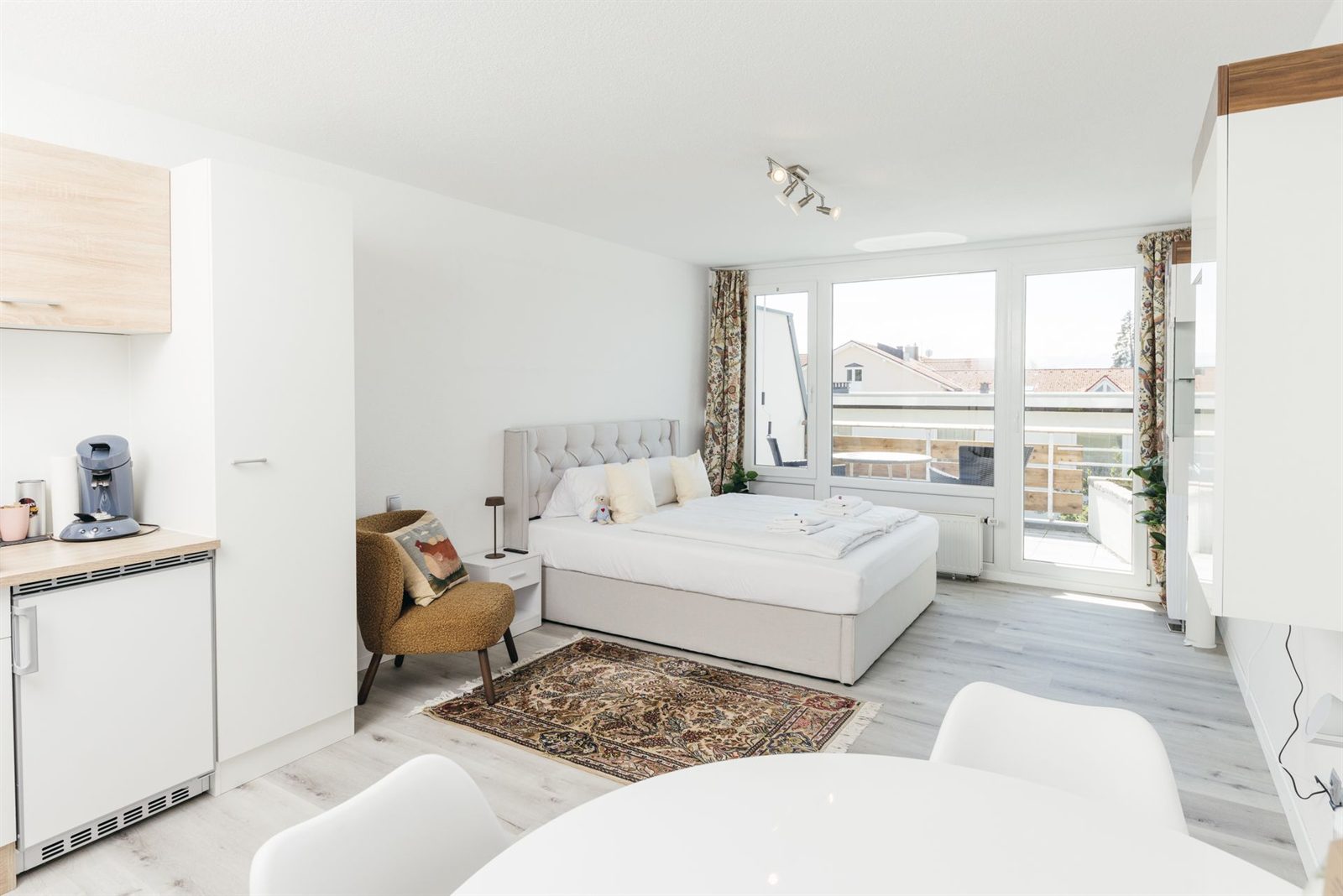 Studio · Vom Esstisch aus über den Teppich hinweg zum Bett und zur Balkontür