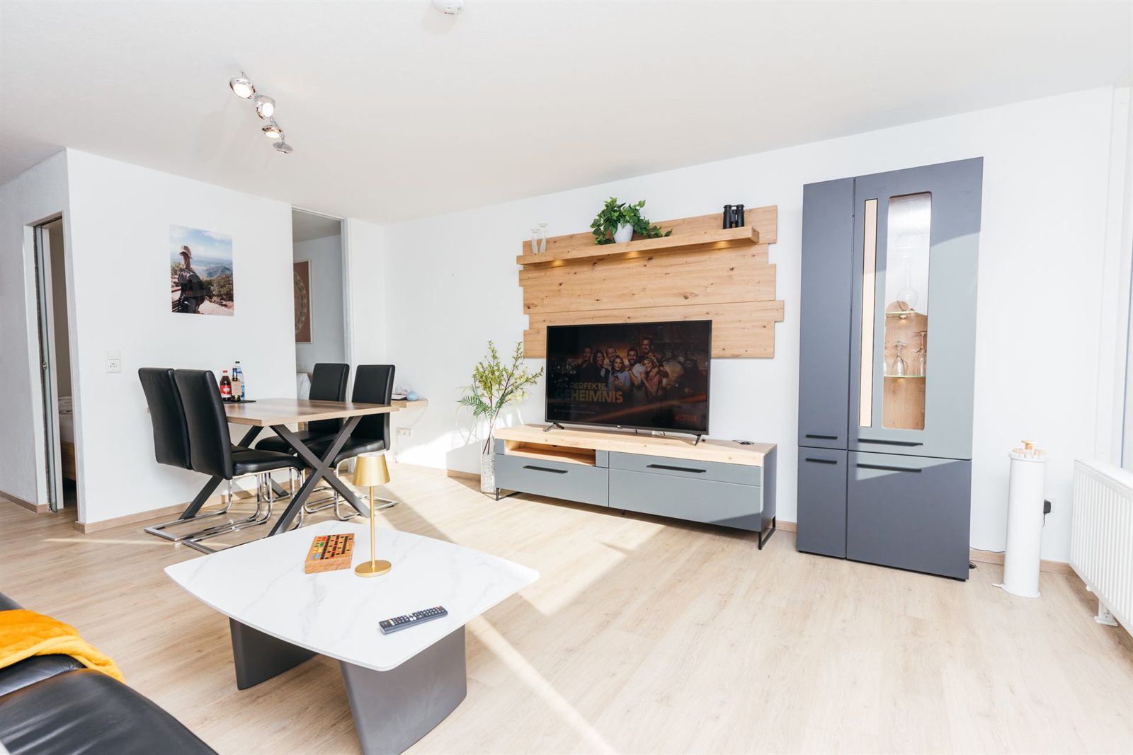 Wohnzimmer · Esstisch für vier, daneben die Wohnwand mit Smart-TV vor Altholz