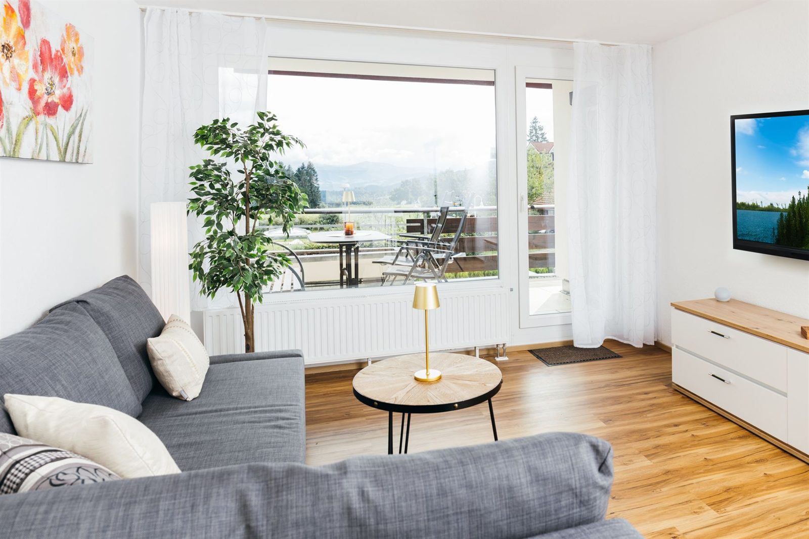 Wohnzimmer · Couchtisch zwischen Sofa und Fenster, draußen warten Tisch und Liegestühle